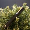 CRKT CEO folding knife closed, resting on green foliage, showing the deep-carry pocket clip
